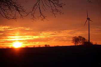 Silhouette of wind turbine against vibrant orange sunrise sky