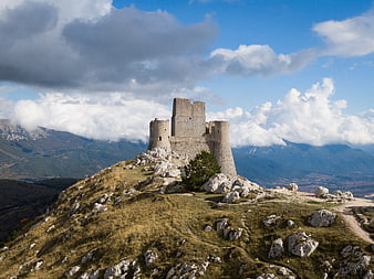 Medieval stone castle ruins on a rocky mountain peak with dramatic clouds