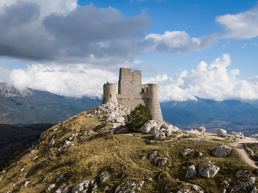 Medieval stone castle ruins on a rocky mountain peak with dramatic clouds