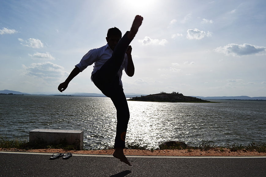 Silhouette of man performing high kick martial arts by lake