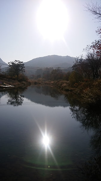 Serene River Landscape with Sun Flare and Mountain Reflection