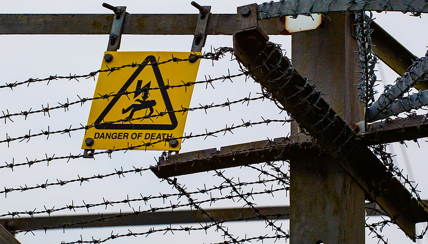 Danger of death warning sign behind barbed wire fence