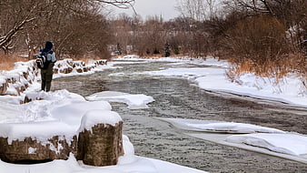Man with Backpack Standing by Snowy Winter River