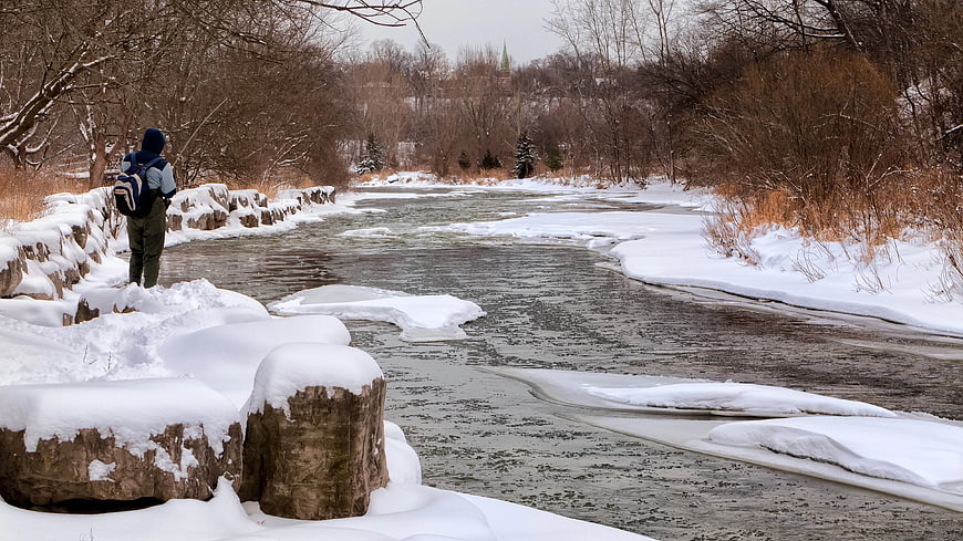 Man with Backpack Standing by Snowy Winter River