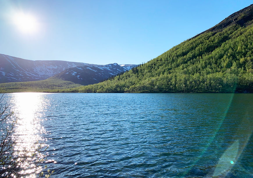 Serene Mountain Lake with Sunlight and Forested Hills