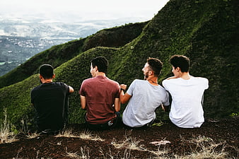 Four male friends sitting on a mountain ridge overlooking a valley