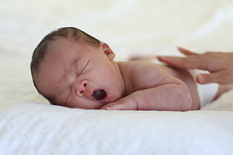 Newborn Baby Yawning On White Bedding With Parent Hand