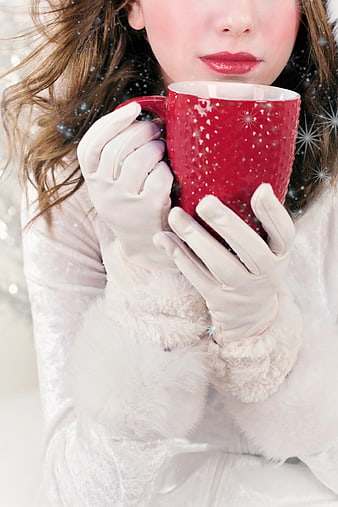 Woman in white winter coat holding red festive mug in snow