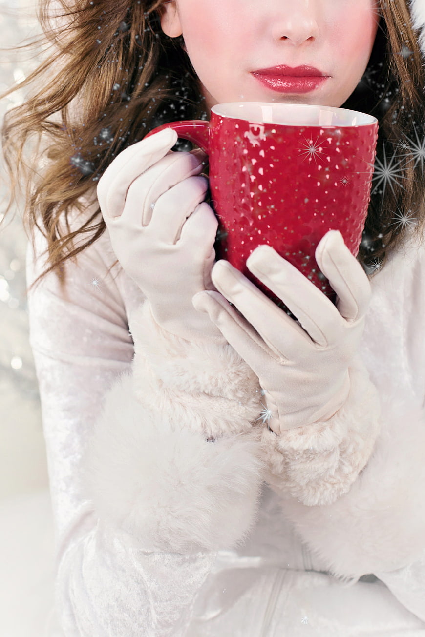 Woman in white winter coat holding red festive mug in snow