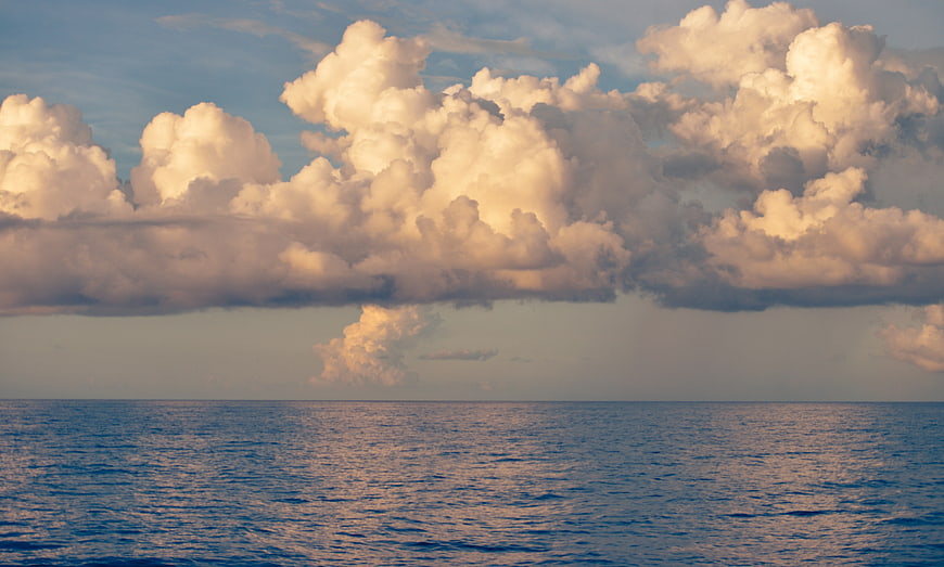 Golden Sunlit Cumulus Clouds Over Calm Blue Ocean Horizon