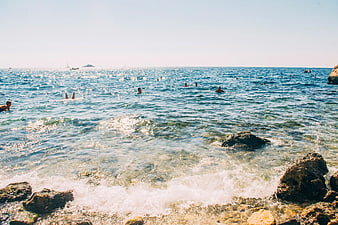 People swimming in sparkling blue ocean near rocky shore