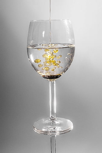 Clear liquid pouring into a wine glass with golden bubbles on a gray background