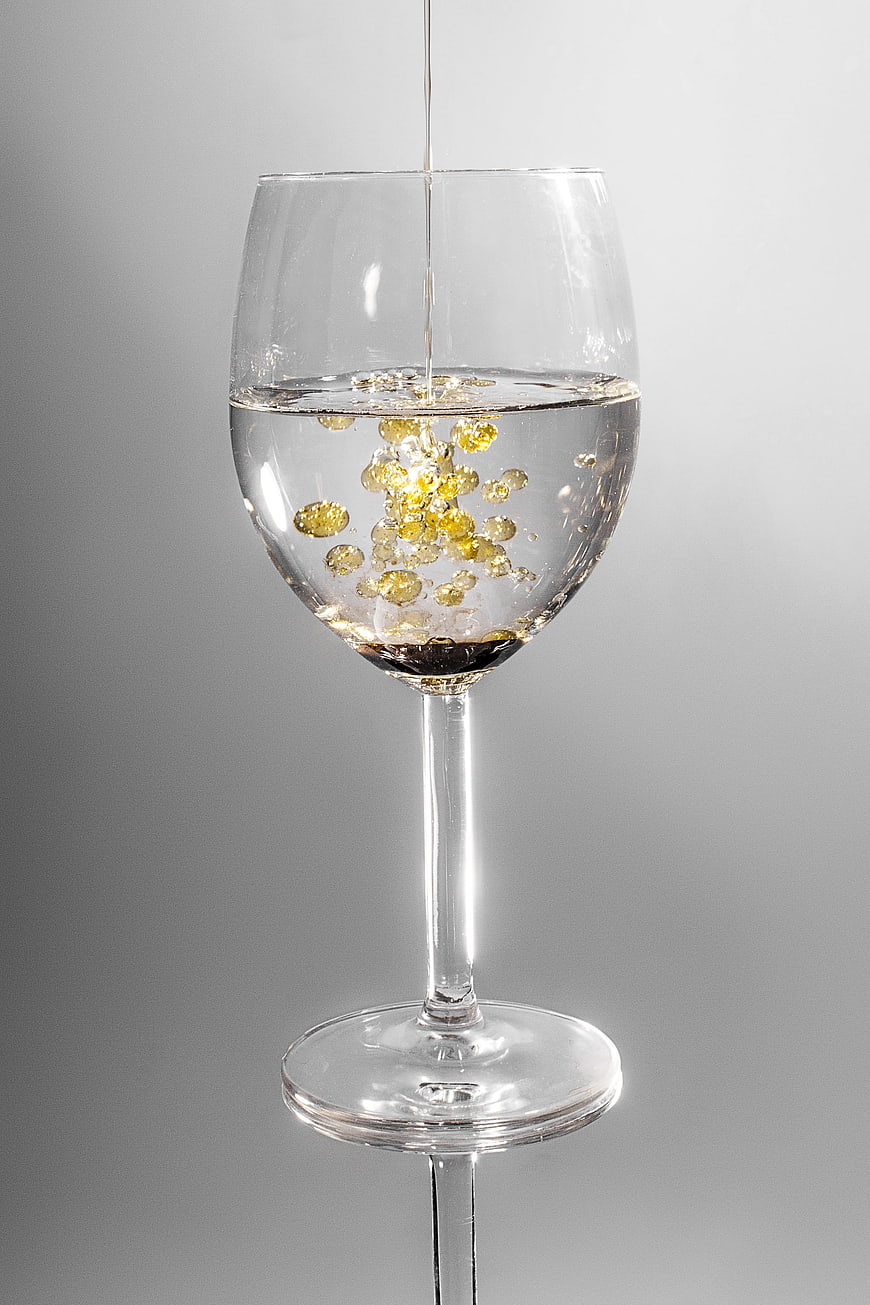 Clear liquid pouring into a wine glass with golden bubbles on a gray background