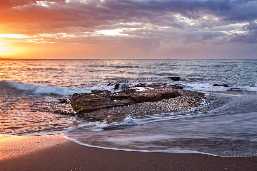 Dramatic Sunset Over Rocky Beach with Long Exposure Waves