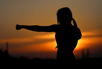 Silhouette of woman practicing martial arts at sunset