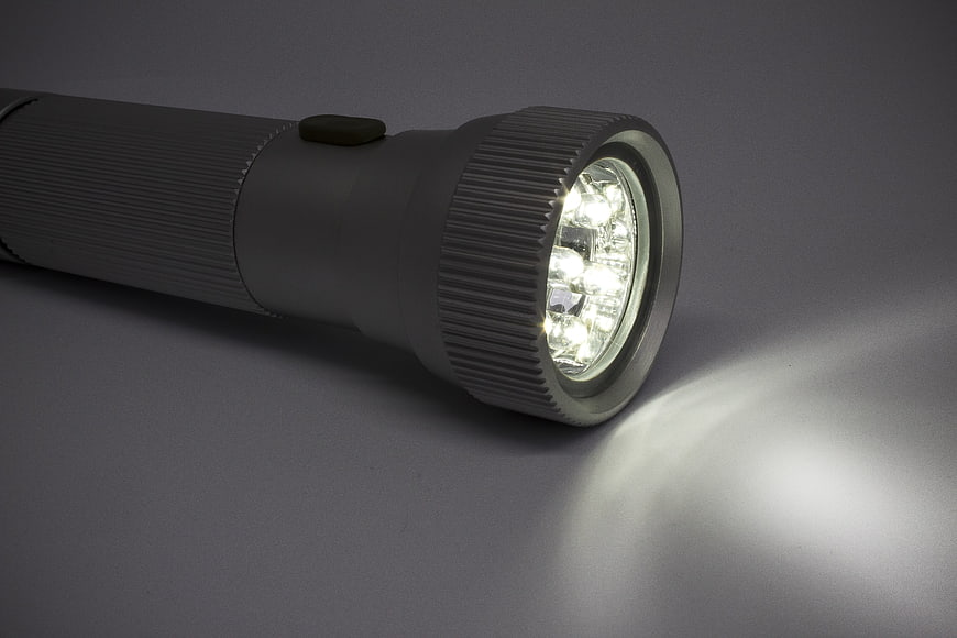 Illuminated LED Flashlight Close-Up On Gray Background
