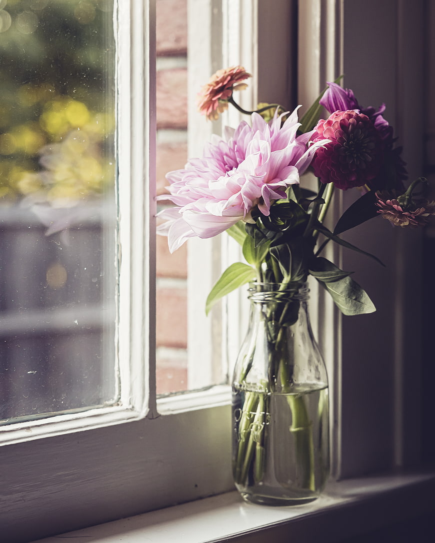 Pink and purple flowers in a glass bottle on a windowsill