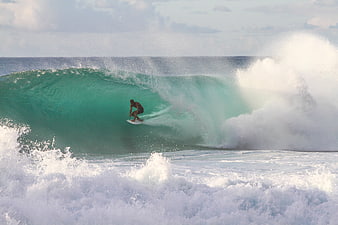 Surfer riding inside a large turquoise ocean wave barrel
