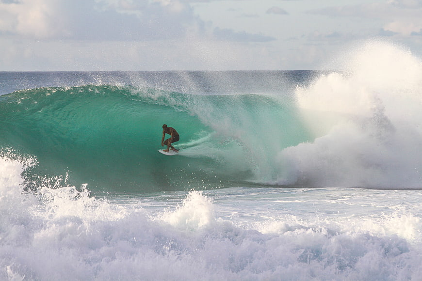 Surfer riding inside a large turquoise ocean wave barrel
