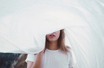 Woman holding white fabric over face outdoors