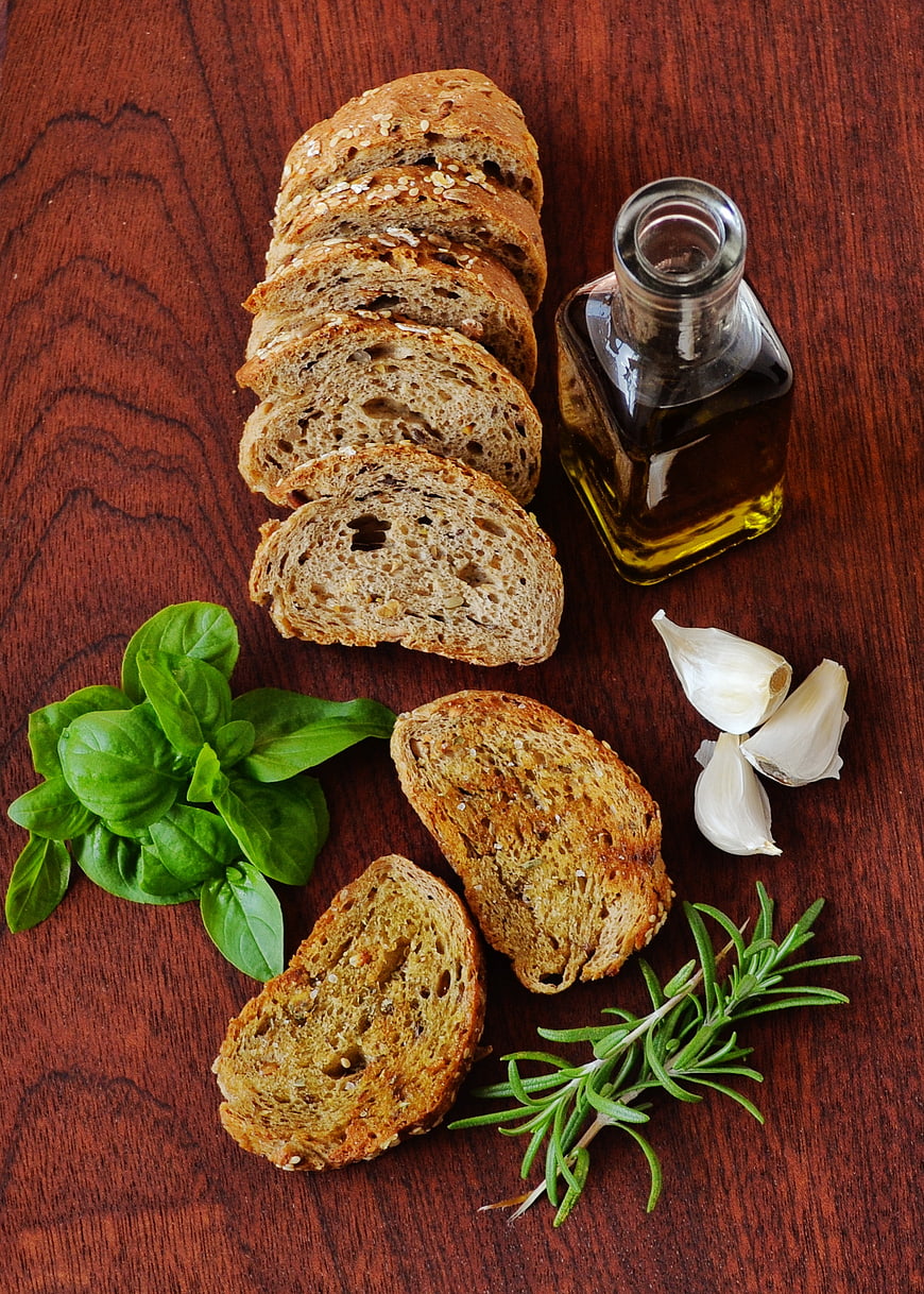 Sliced whole grain bread with olive oil, basil, and rosemary on wood