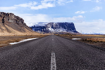 Empty asphalt road leading to snow-capped mountains in Iceland