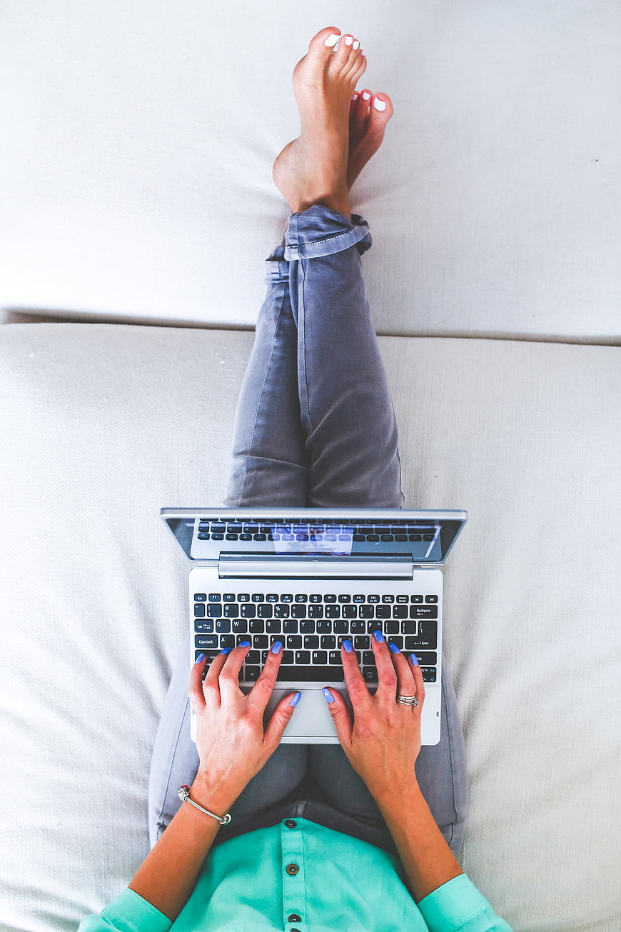 Top view of woman typing on laptop while lying on sofa