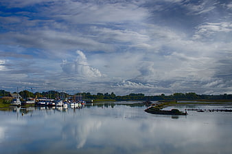 Panoramic View of Boats Docked in a River with Cloudy Sky Reflection
