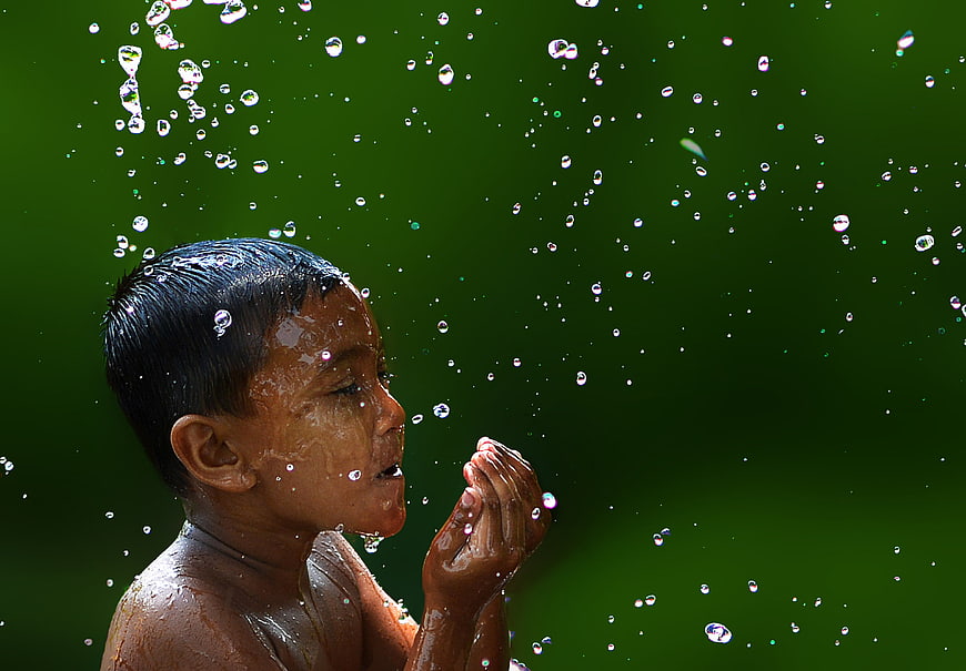 Young boy drinking water from cupped hands against green background