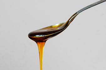 Golden Honey Dripping from Silver Spoon on White Background