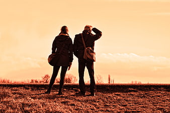 Couple standing in field looking at sunset horizon