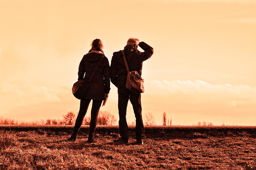 Couple standing in field looking at sunset horizon