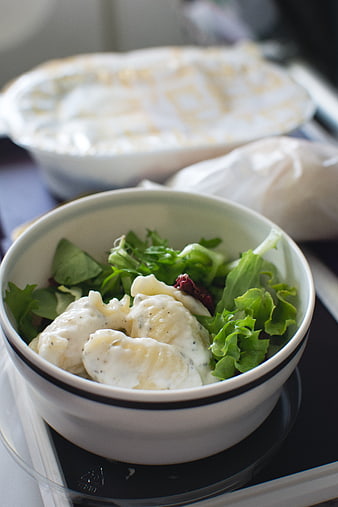 Close-up of creamy gnocchi salad in a white bowl on an airplane tray