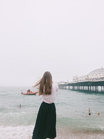 Woman in Black Skirt Looking at Brighton Pier on Overcast Day