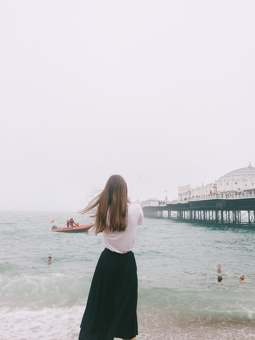 Woman in Black Skirt Looking at Brighton Pier on Overcast Day