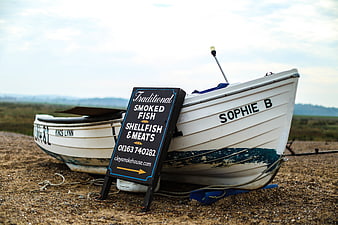 Smoked Fish Sign Leaning Against White Fishing Boat on Beach