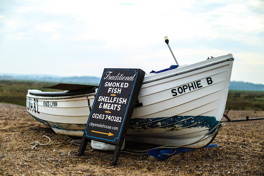 Smoked Fish Sign Leaning Against White Fishing Boat on Beach