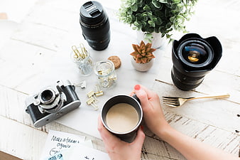 Flat lay of camera lenses, vintage camera, and coffee on white desk