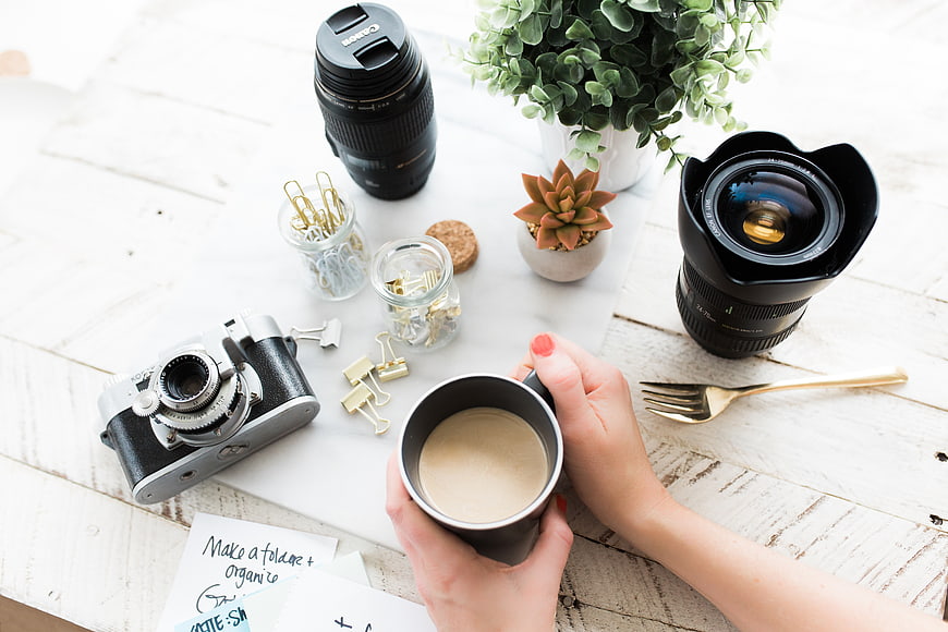 Flat lay of camera lenses, vintage camera, and coffee on white desk