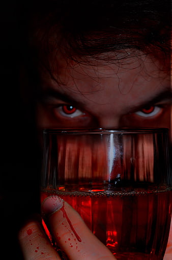 Close-up of a man with red eyes holding a glass of red liquid