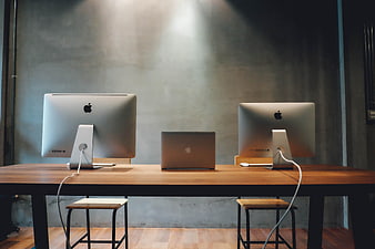 Modern Workspace with Two iMacs and Laptop on Wooden Desk