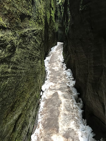Narrow rocky canyon path with snow and mossy walls