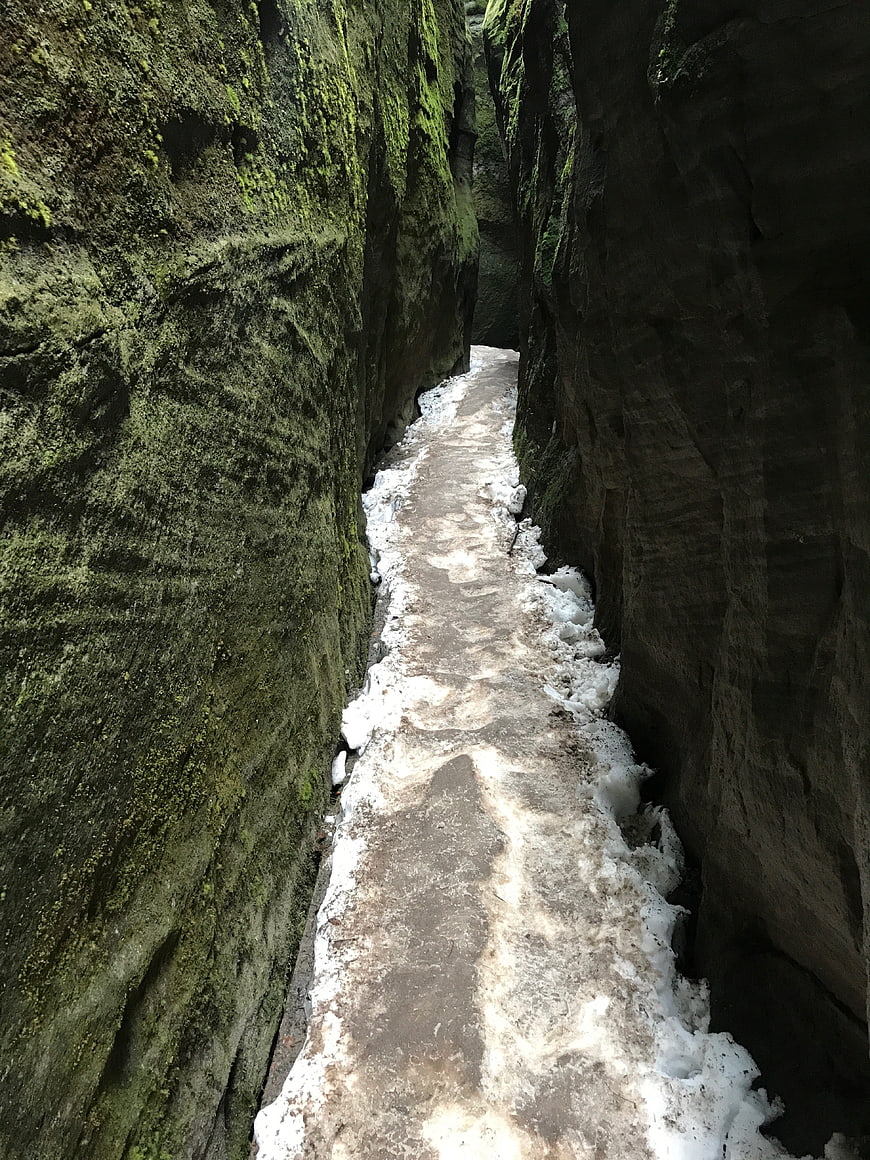 Narrow rocky canyon path with snow and mossy walls