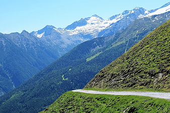 Winding mountain road through green alpine valley with snowy peaks