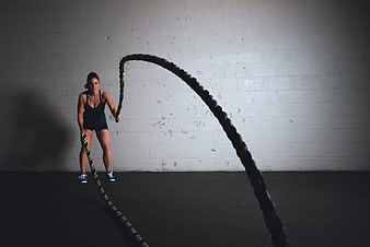 Female Athlete Performing Battle Rope Workout In Gym