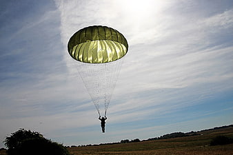 Paratrooper Landing With Green Parachute Over Rural Fields