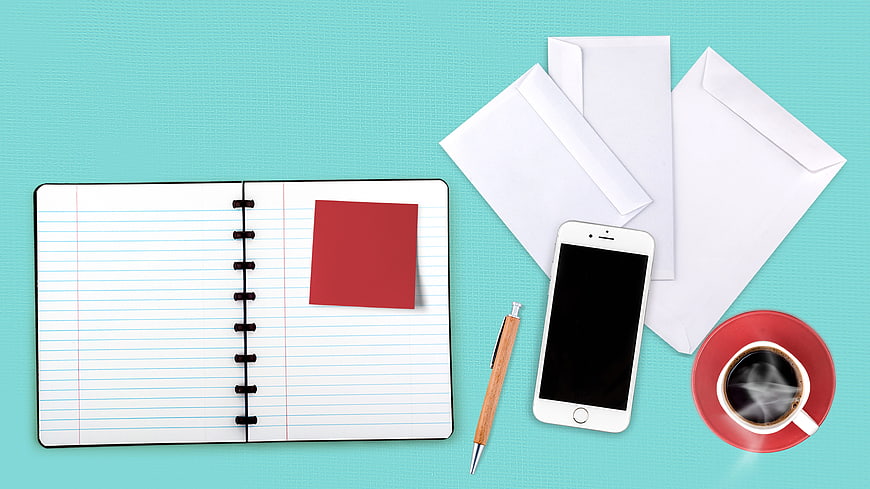 Flat lay of open notebook, smartphone, envelopes, pen, and coffee on teal background
