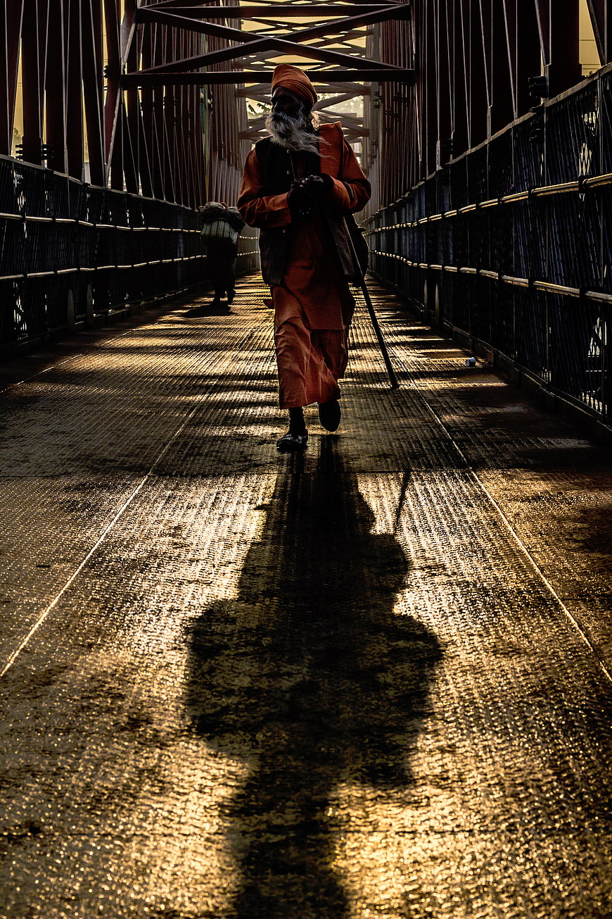 Sikh man walking on bridge with long shadow