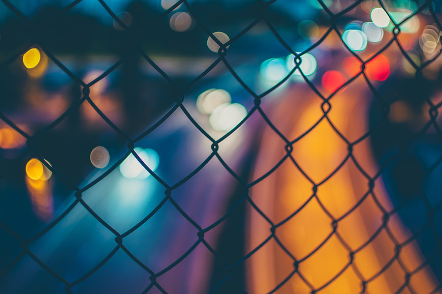 Chain link fence with colorful bokeh lights at night