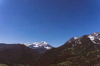 Snow-Capped Mountain Peak with Forested Slopes and Blue Sky